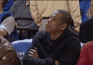 A Man In A Black Hoodie Is Sitting In A Crowd Of People Watching A Game . GIF