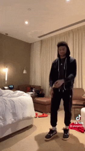 A Man In A Black Hoodie Is Standing In A Hotel Room With Tiktok Written On The Bottom GIF