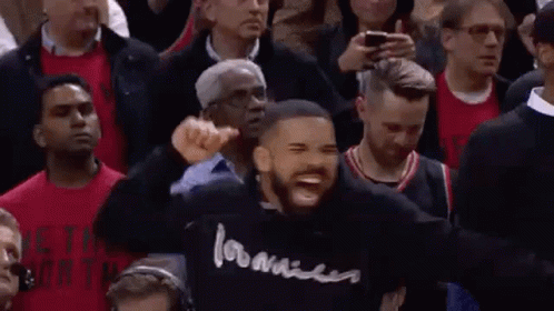 A Man In A Black Hoodie Is Standing In Front Of A Crowd Of People . GIF
