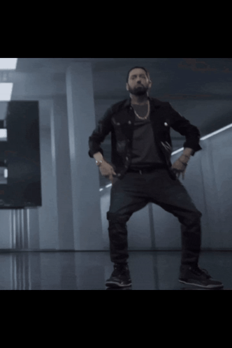 A Man In A Black Jacket And Black Pants Is Dancing In A Dark Room GIF
