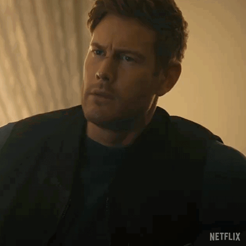 A Man In A Black Jacket And Black Shirt Is Sitting On A Couch And Looking At The Camera . GIF