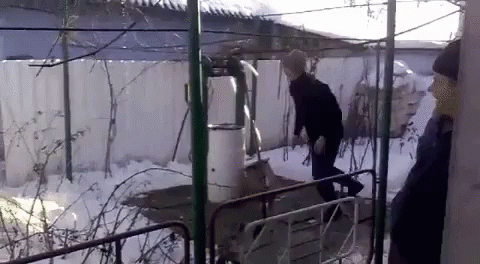 A Man In A Black Jacket And Hat Is Standing In The Snow GIF