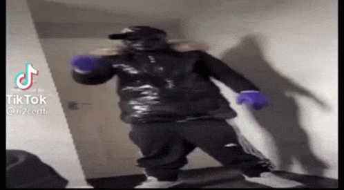 A Man In A Black Jacket And Purple Gloves Is Standing In A Room . GIF