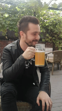 A Man In A Black Jacket Drinks From A Glass With The Letter N On It GIF