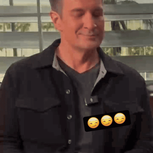 A Man In A Black Jacket Has Three Smiley Faces On His Shirt GIF
