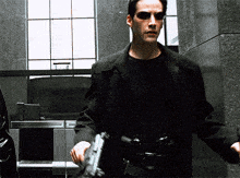A Man In A Black Jacket Holds A Gun GIF