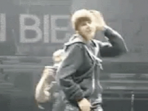 A Man In A Black Jacket Is Dancing On A Stage In Front Of A Sign That Says I Bie . GIF