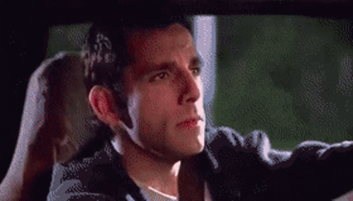 A Man In A Black Jacket Is Driving A Car And Looking Out The Window GIF