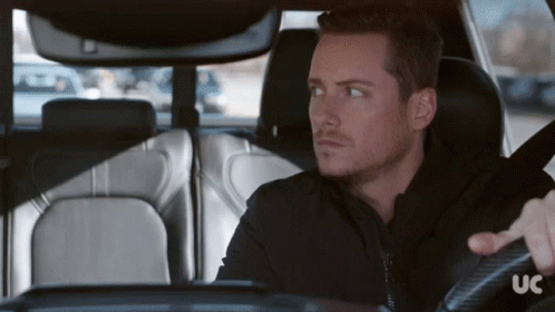 A Man In A Black Jacket Is Driving A Car With The Letters Uc On The Steering Wheel GIF