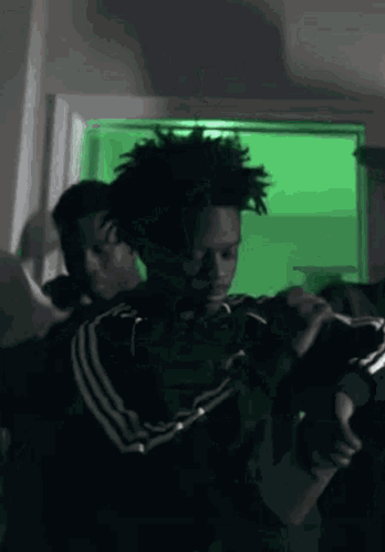A Man In A Black Jacket Is Holding A Gun In A Room With A Green Background . GIF