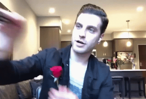 A Man In A Black Jacket Is Holding A Red Rose In His Hands GIF