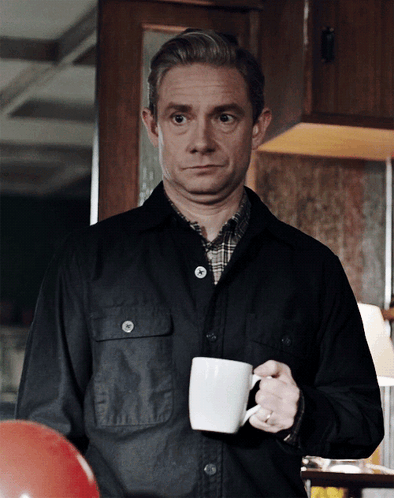 A Man In A Black Jacket Is Holding A White Coffee Cup GIF