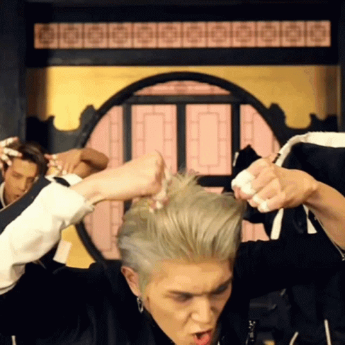 A Man In A Black Jacket Is Holding His Hair In A Circle GIF