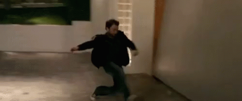 A Man In A Black Jacket Is Kneeling Down In A Hallway . GIF