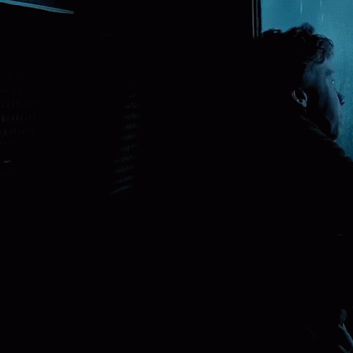 a man in a black jacket is looking out a window with his hand on the glass