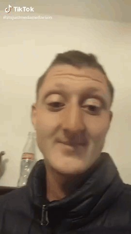 A Man In A Black Jacket Is Making A Funny Face In Front Of A Bottle Of Soda . GIF