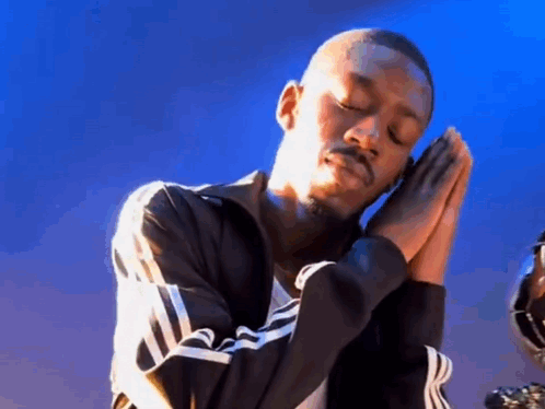 A Man In A Black Jacket Is Praying With His Hands Folded . GIF