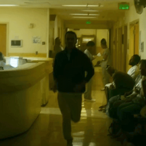 A Man In A Black Jacket Is Running Down A Hallway GIF