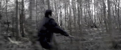 A Man In A Black Jacket Is Running Through A Dark Forest . GIF