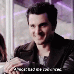 A Man In A Black Jacket Is Sitting At A Table And Smiling While Saying `` Almost Had Me Convinced . '' GIF