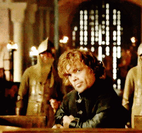 A Man In A Black Jacket Is Sitting At A Table With His Hands Folded GIF