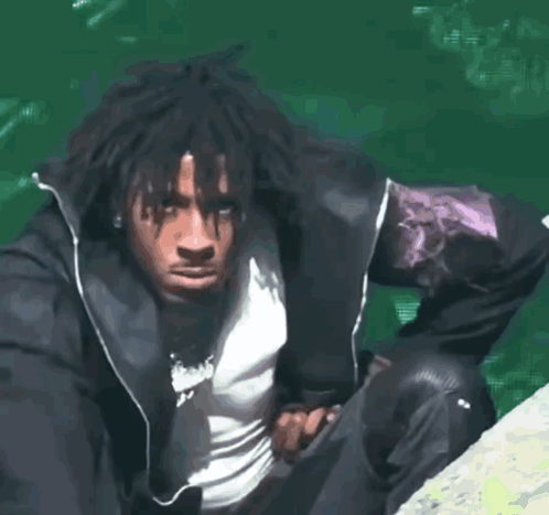 A Man In A Black Jacket Is Sitting On A Rock Near A Body Of Water GIF