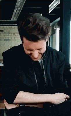 A Man In A Black Jacket Is Smiling And Looking Down GIF