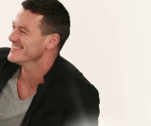 A Man In A Black Jacket Is Smiling And Looking To The Side . GIF