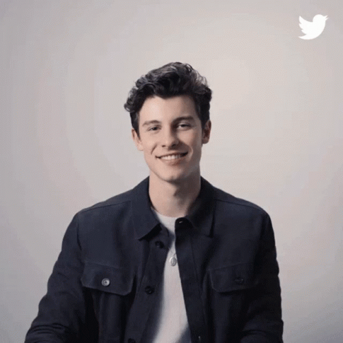 A Man In A Black Jacket Is Smiling In Front Of A Twitter Icon GIF