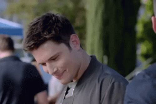A Man In A Black Jacket Is Smiling While Standing Next To Another Man . GIF