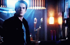 A Man In A Black Jacket Is Standing In A Dark Room Looking At The Camera GIF