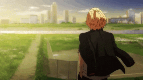 A Man In A Black Jacket Is Standing In A Field Looking At A City Skyline GIF