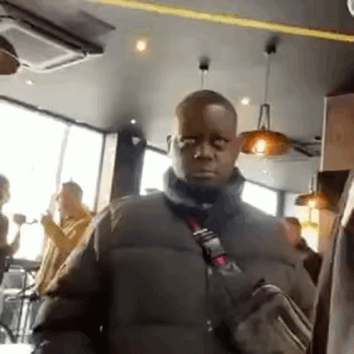A Man In A Black Jacket Is Standing In A Restaurant With A Bag On His Shoulder . GIF