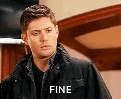 A Man In A Black Jacket Is Standing In A Room With The Word Fine Written On His Chest . GIF