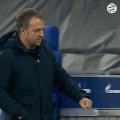 A Man In A Black Jacket Is Standing In Front Of A Blue Box That Says Fc Bayern Munich GIF