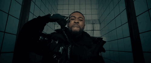 A Man In A Black Jacket Is Standing In Front Of A Blue Tiled Wall GIF