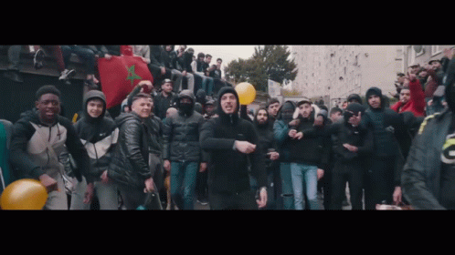 A Man In A Black Jacket Is Standing In Front Of A Crowd Of People GIF