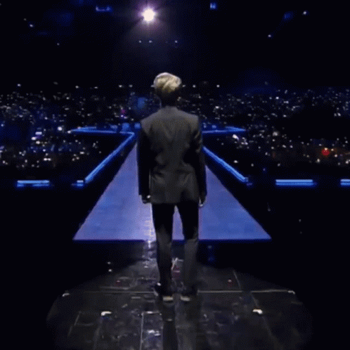A Man In A Black Jacket Is Standing In Front Of A Field Of Skulls GIF