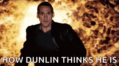A Man In A Black Jacket Is Standing In Front Of A Fire . GIF