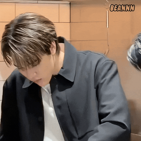 A Man In A Black Jacket Is Standing In Front Of A Wall With Beannn Written On It GIF