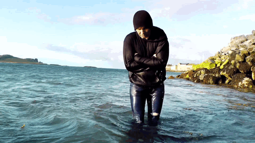 A Man In A Black Jacket Is Standing In The Water GIF