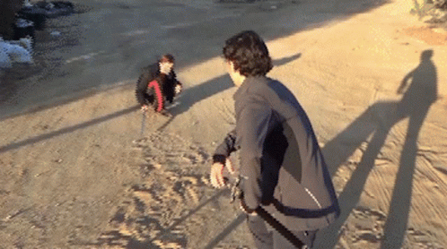 A Man In A Black Jacket Is Standing On A Dirt Road Next To Another Man GIF