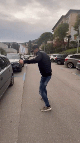 A Man In A Black Jacket Is Standing On The Side Of A Road GIF