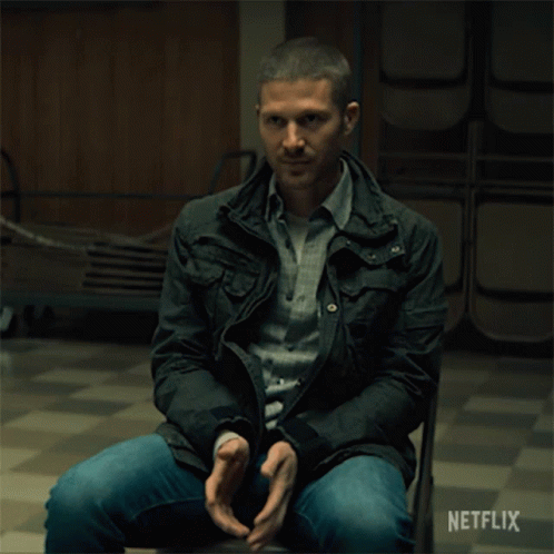 A Man In A Black Jacket Sits In A Chair With A Netflix Logo On The Bottom GIF