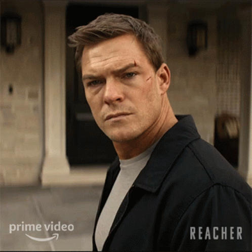 A Man In A Black Jacket Stands In Front Of A Building With Reacher Written On It GIF