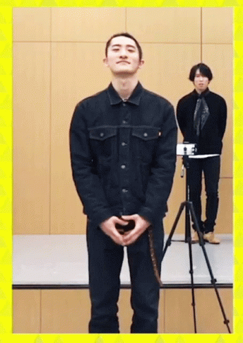 A Man In A Black Jacket Stands In Front Of A Camera GIF
