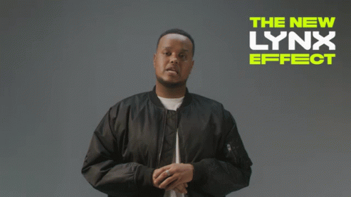 A Man In A Black Jacket Stands In Front Of A Sign That Says " The New Lynx Effect " GIF