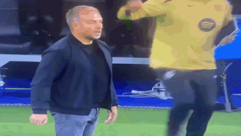 A Man In A Black Jacket Stands Next To A Man In A Yellow Nike Shirt GIF