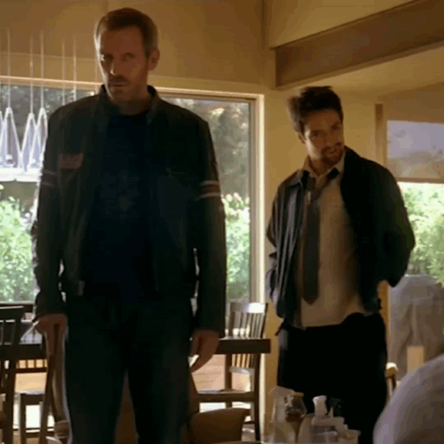 A Man In A Black Jacket Stands Next To Another Man GIF