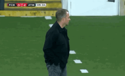 A Man In A Black Jacket Stands On A Soccer Field With The Scoreboard Showing Fcb 0 2 Atm GIF